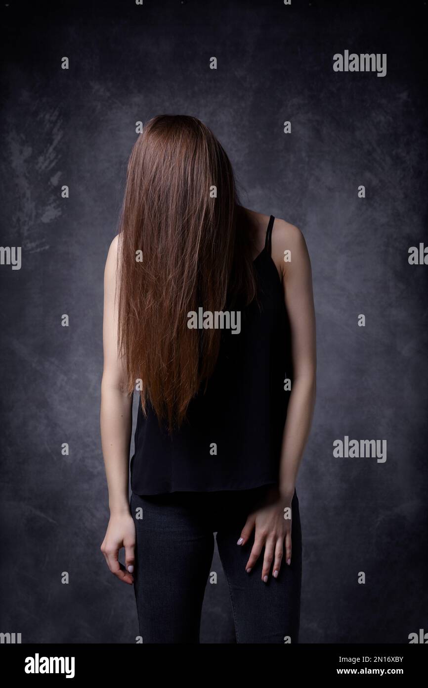 Giovane donna con capelli lisci lunghi. I capelli coprono il viso. Sfondo grigio. Foto Stock
