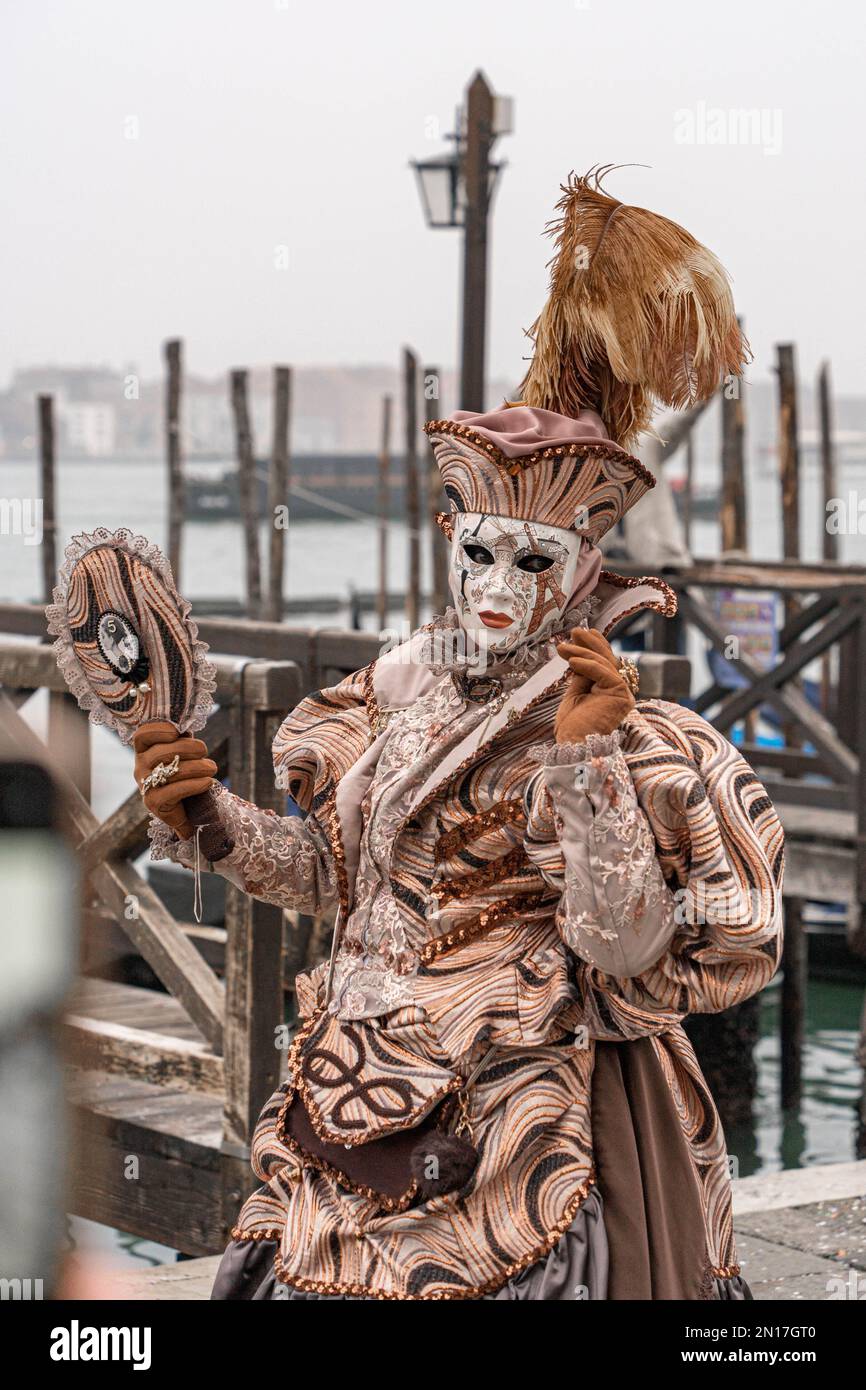 Una donna in costume da carnevale, una maschera, un cappello con piume, uno specchio in mano, si trova sullo sfondo del molo e della Basilica Foto Stock