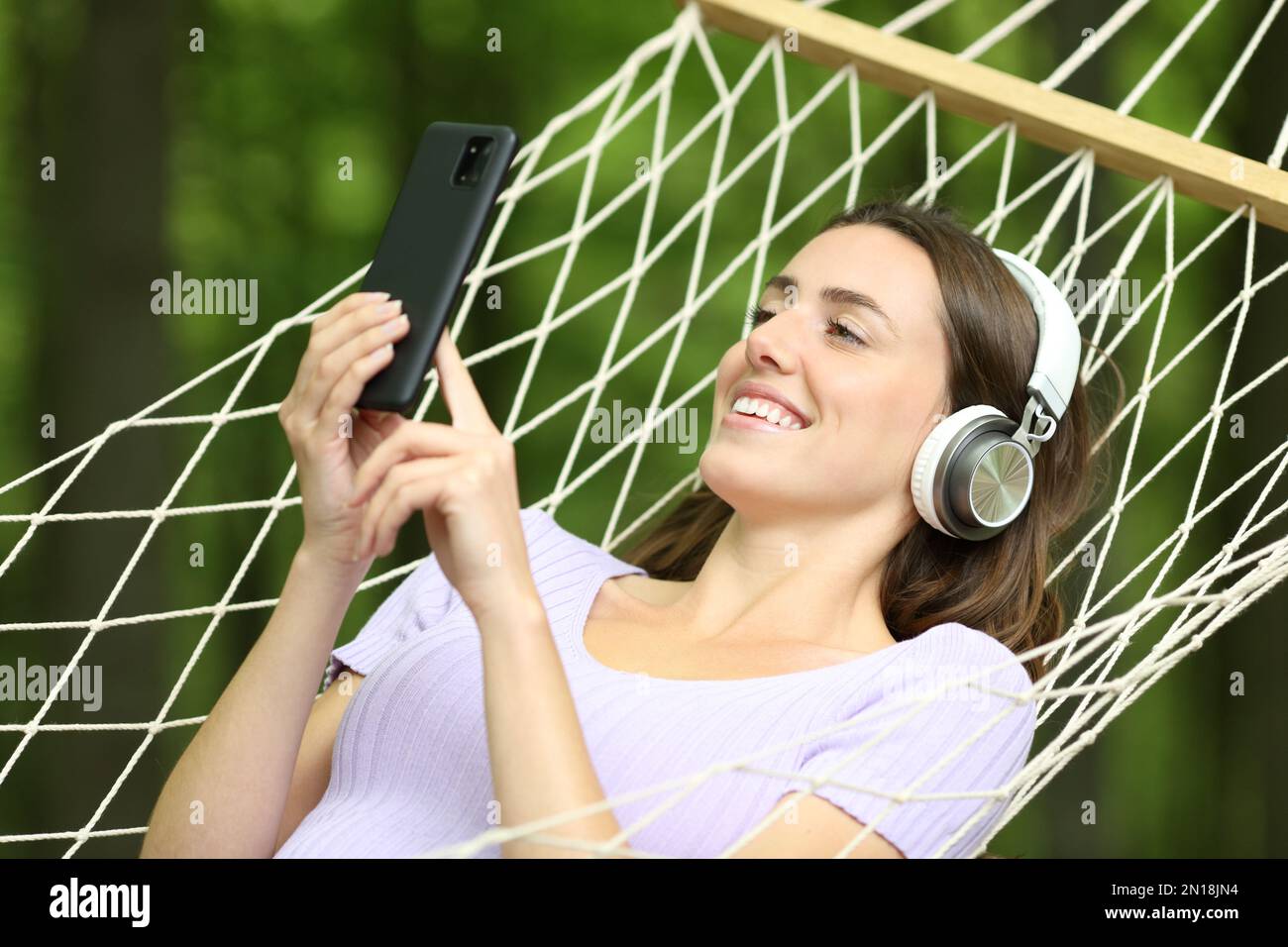 Donna felice su amaca ascoltare musica in una foresta verde Foto Stock