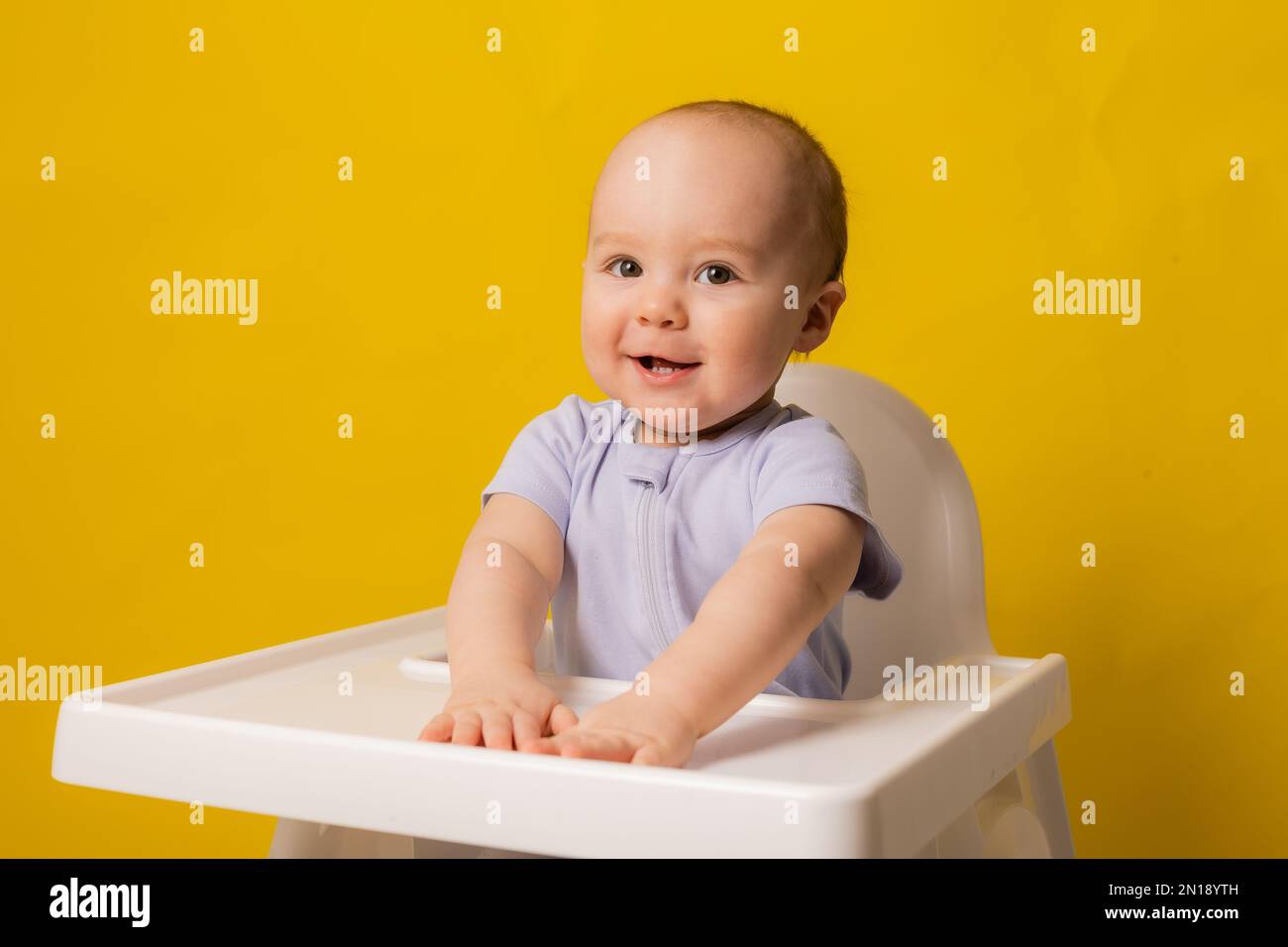 un bambino cute sta sedendosi nella sedia del bambino che gioca su uno sfondo giallo. spazio per il testo, mockup. Foto di alta qualità Foto Stock