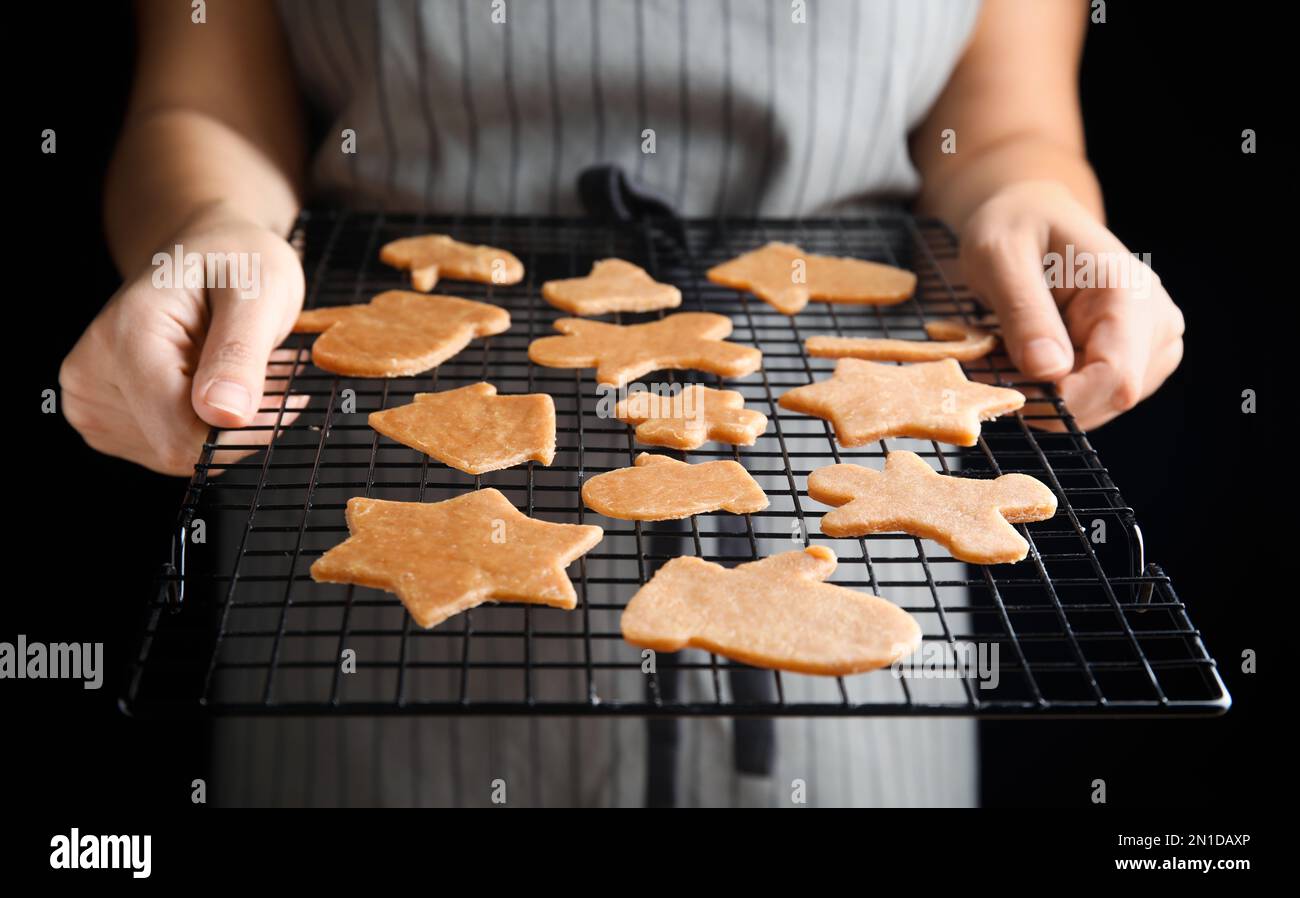 Donna che tiene griglia da forno con biscotti di Natale non cotti su sfondo nero, primo piano Foto Stock