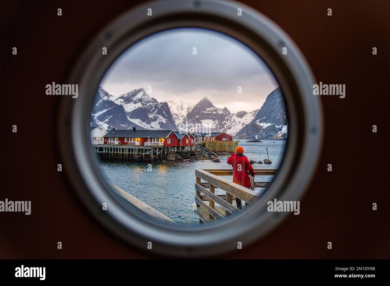 Vista posteriore della persona che guarda le tradizionali cabine di Rorbu attraverso un oblò, Reine Bay, Lofoten Islands, Norway, Scandinavia, Europa Foto Stock