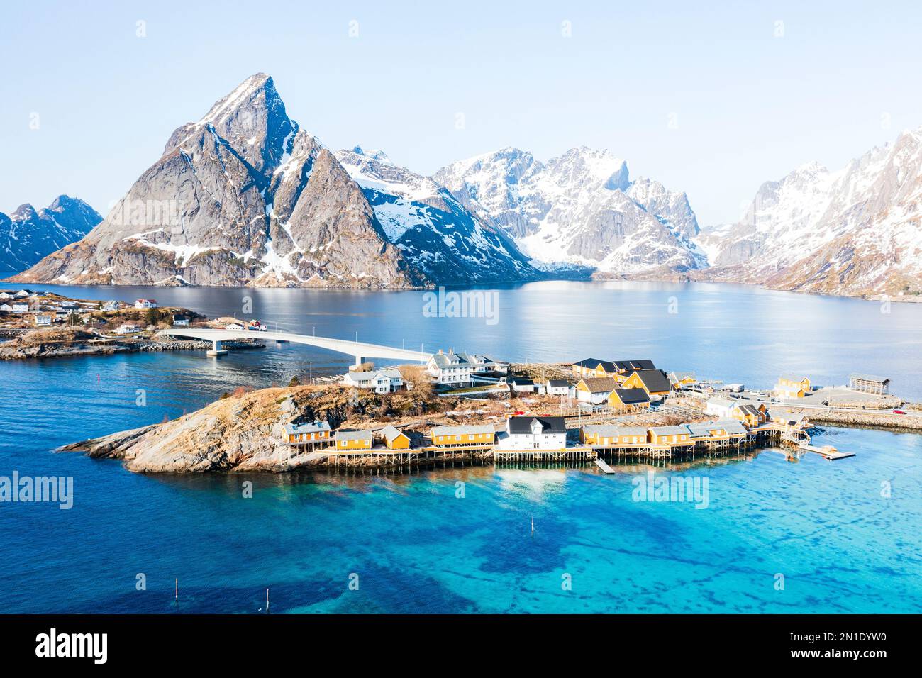 Veduta aerea della cima della montagna di Olstind e del mare turchese che circonda il villaggio di Sakrisoy e la baia di Reine, le isole Lofoten, la Norvegia, la Scandinavia, l'Europa Foto Stock