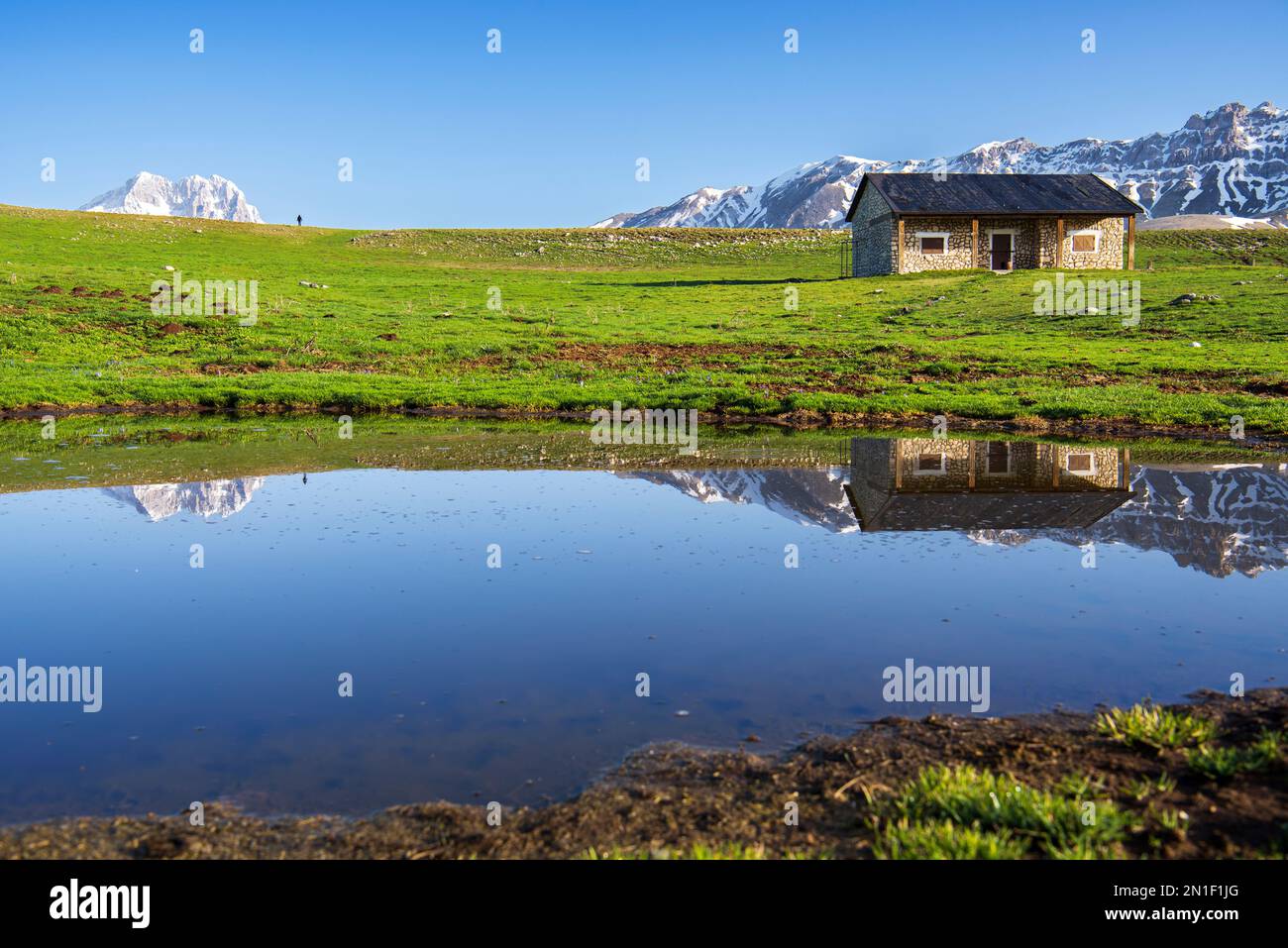 Riflessioni sulla vetta del Gran Sasso e un rifugio tra prati, campo Imperatore, Abruzzo, Appennini, Italia, Europa Foto Stock