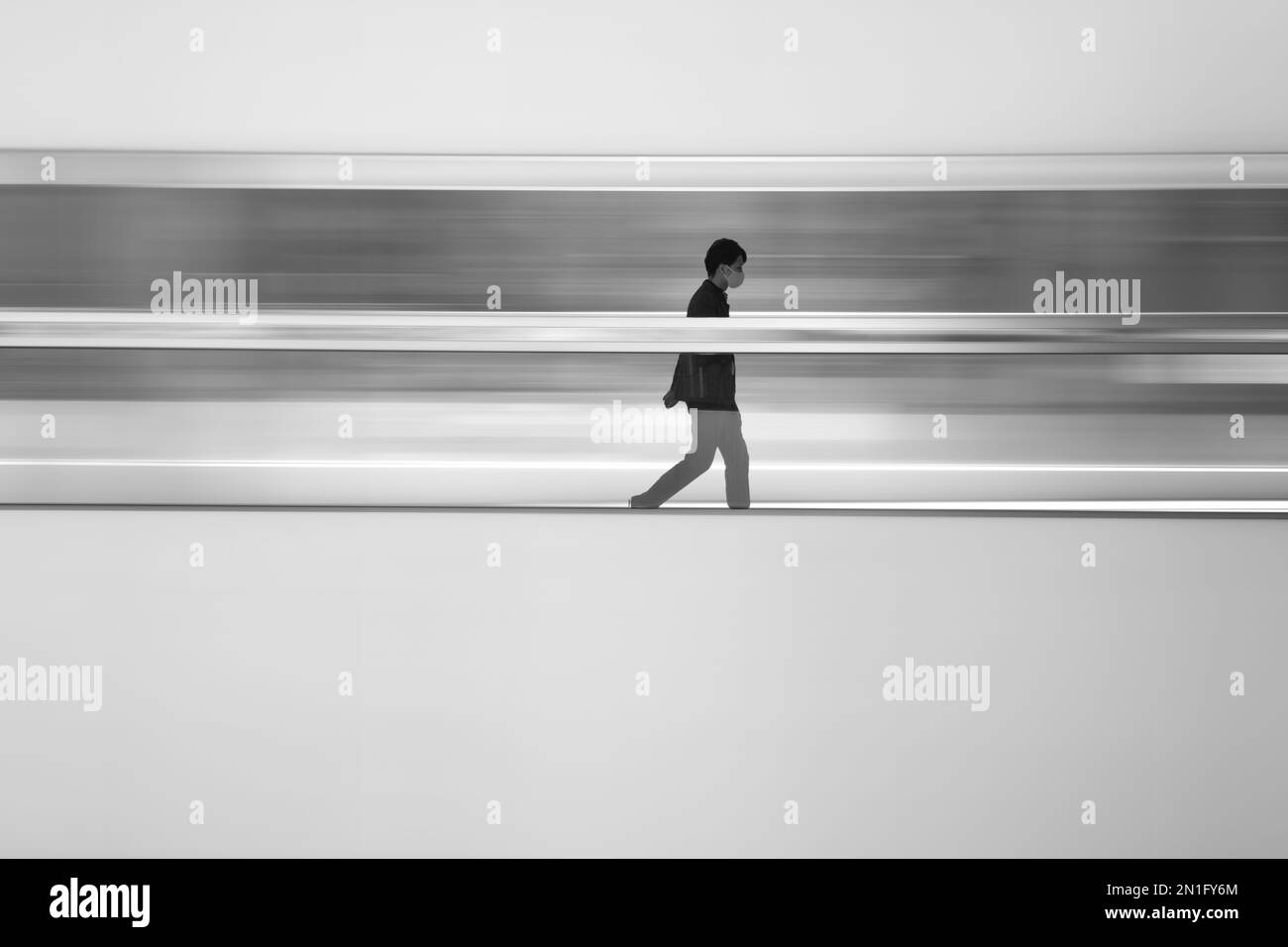 Un uomo isolato cammina attraverso una passerella principale in Central, Hong Kong. È stato aggiunto un effetto di sfocatura allo sfondo. Foto Stock