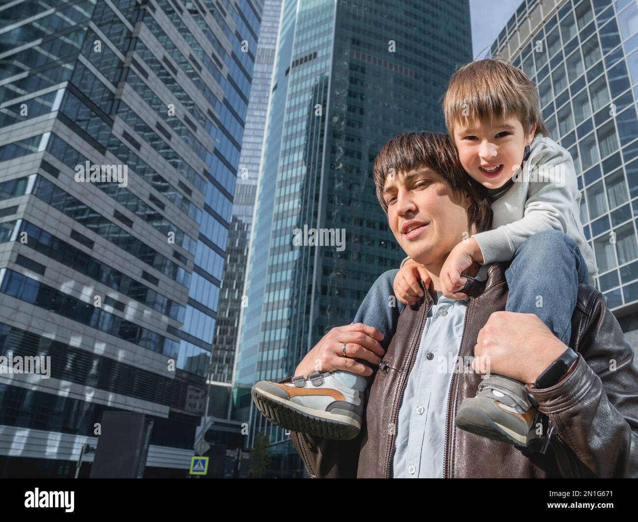 Il ragazzino si siede sulle spalle del padre tra i grattacieli. Papà e figlio guarda su pareti di vetro di edifici. Tecnologie future e moderne, equilibrio di vita Foto Stock