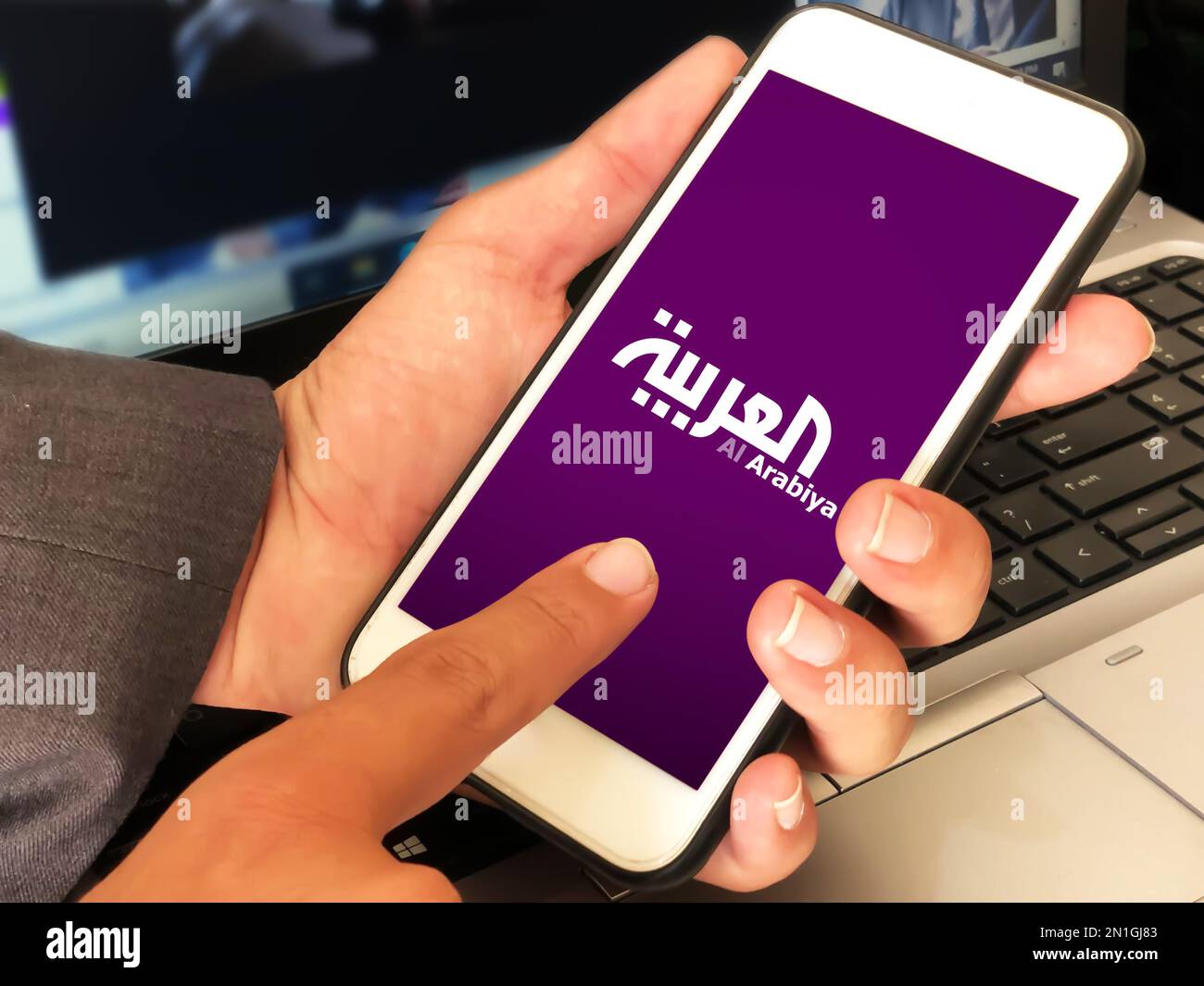 Persona che utilizza l'app mobile delle vie aeree di al arabia con il laptop sullo sfondo, editoriale Foto Stock