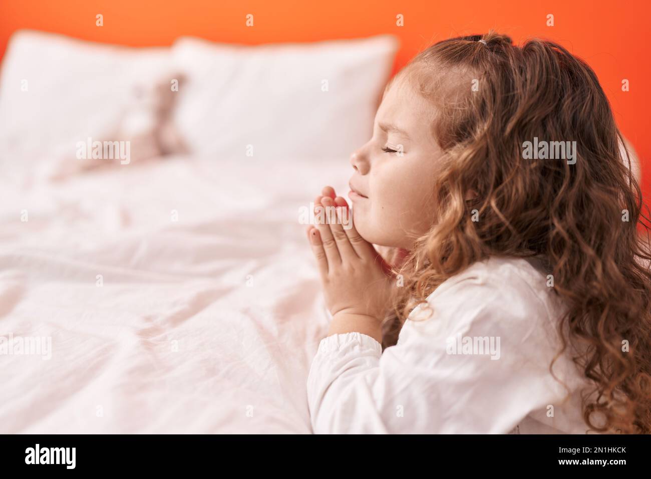 Adorabile bambino biondo che prega seduto al piano della camera da letto Foto Stock