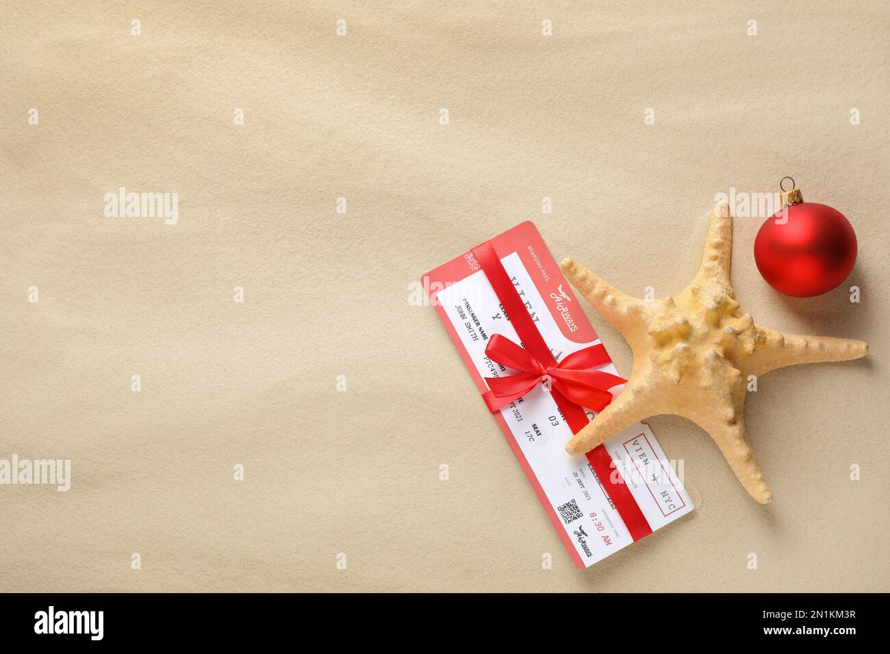 Biglietto aereo con arco rosso, stelle marine, palla di festa e spazio per il testo sulla sabbia, piatto. Vacanze di Natale Foto Stock