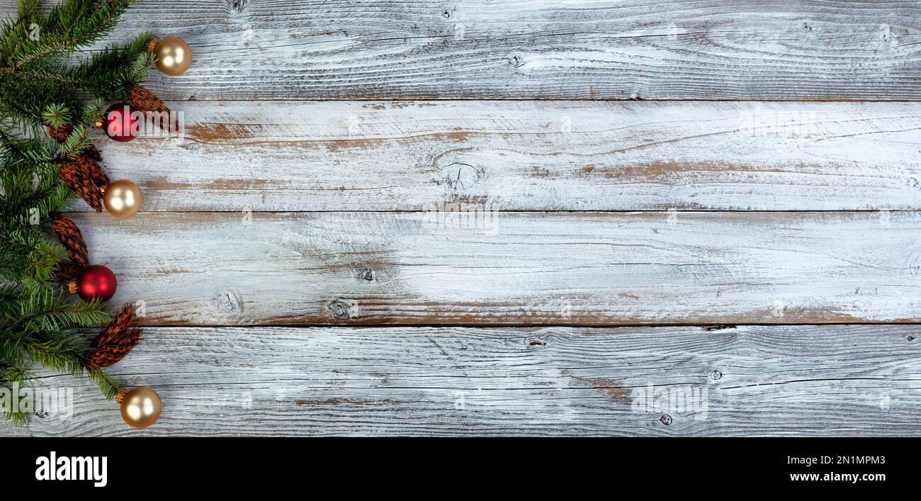 Decorazione natalizia con veri rami di abete più ornamenti rosso e oro palla formando il bordo sinistro su sfondo bianco legno invecchiato Foto Stock