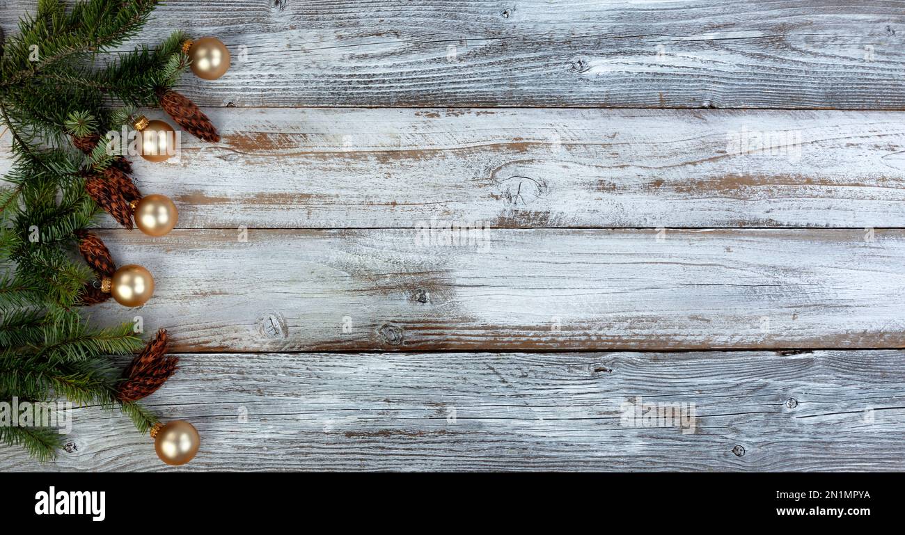 Decorazione di Natale con rami di abete reale più ornamenti di sfera d'oro che formano il bordo sinistro su sfondo bianco di legno invecchiato Foto Stock