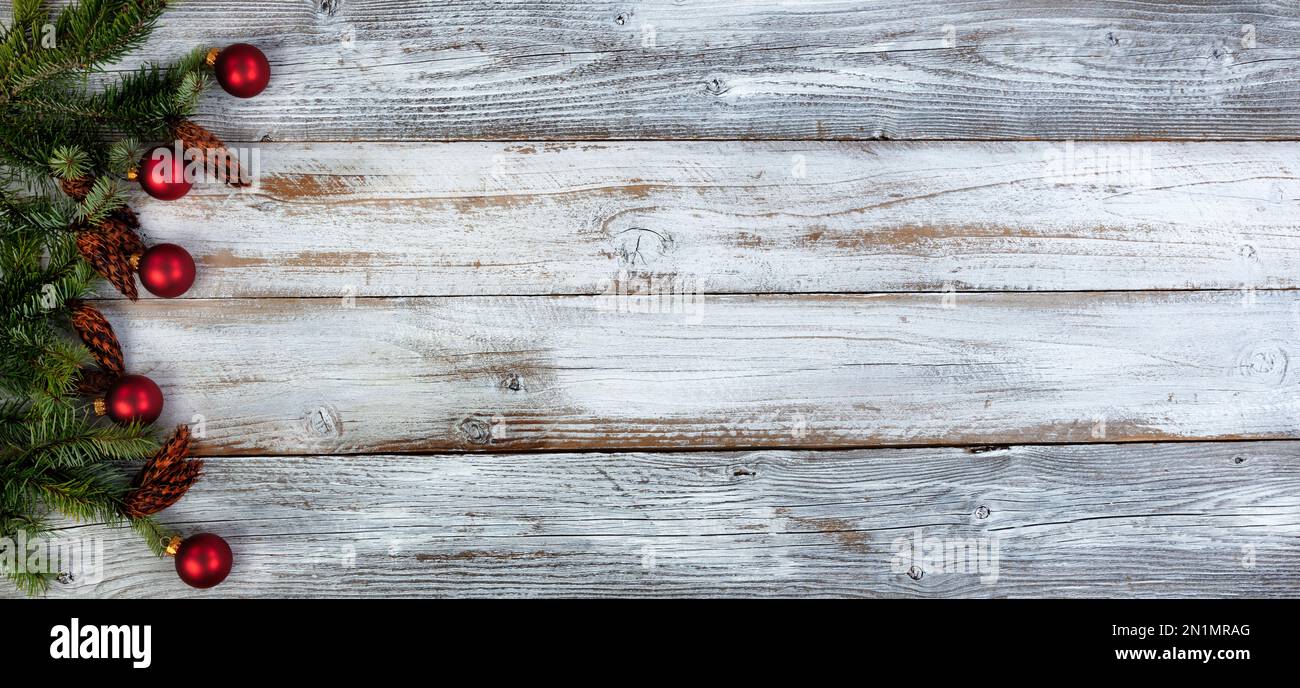 Decorazione natalizia con veri rami di abete e ornamenti di pallina rossa che formano il bordo sinistro su sfondo di legno invecchiato bianco Foto Stock