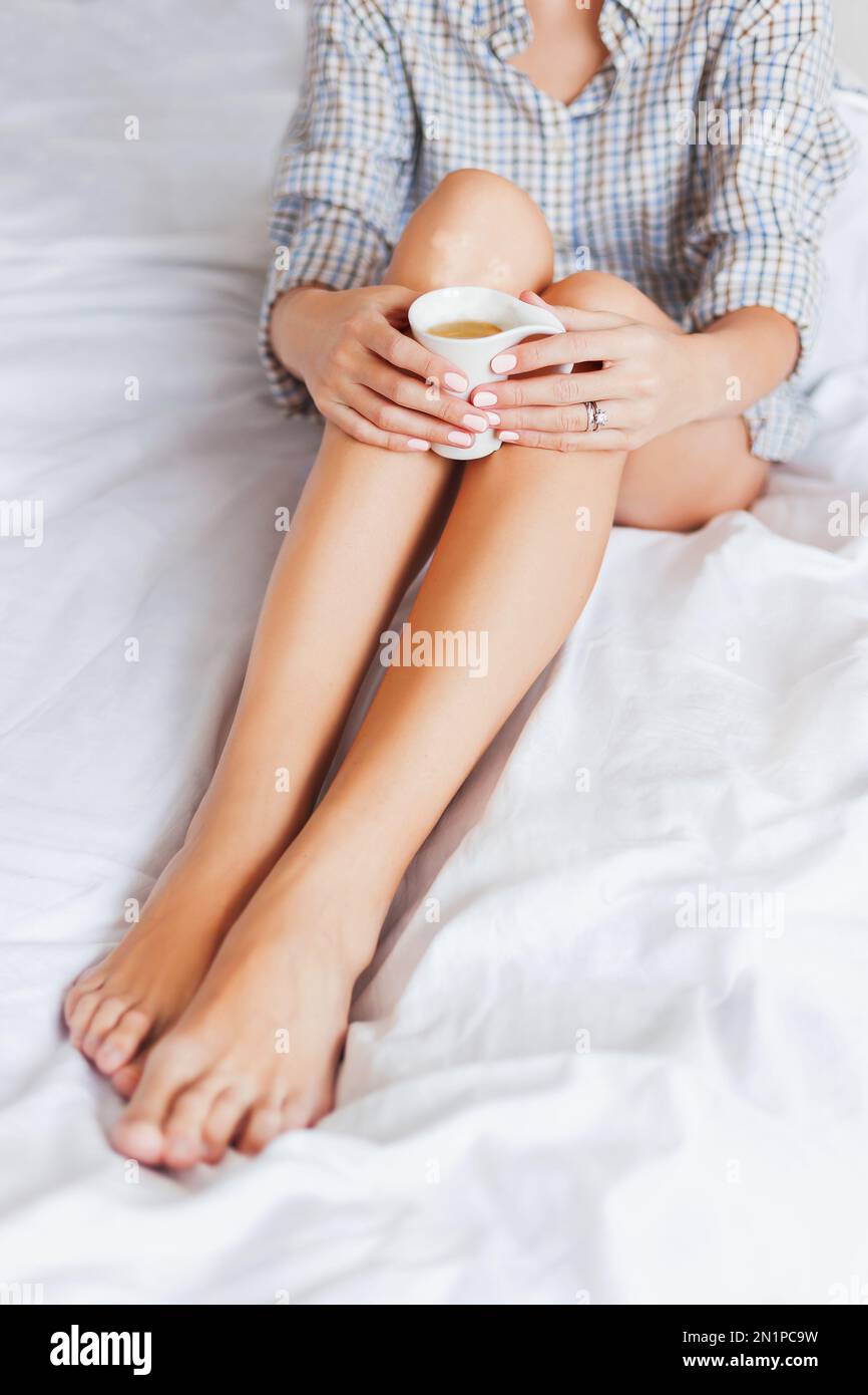 Donna in pajama camicia seduta a letto con tazza di caffè caldo. Routine mattutina accogliente. Stile di vita lento. Foto Stock