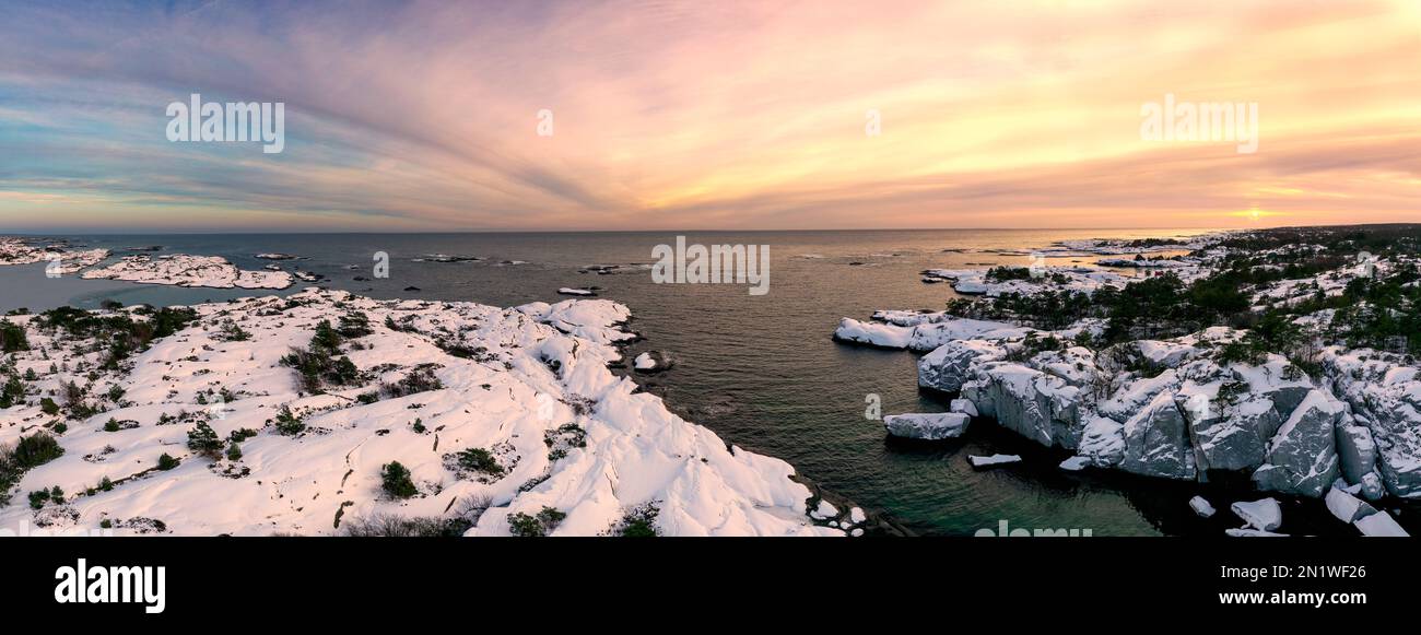 Vista aerea della costa innevata del mare, cielo colorato al tramonto in Norvegia. Paesaggio solare invernale con ghiaia gelida, fiordo e linea dell'orizzonte. Vista dall'alto. Foto Stock
