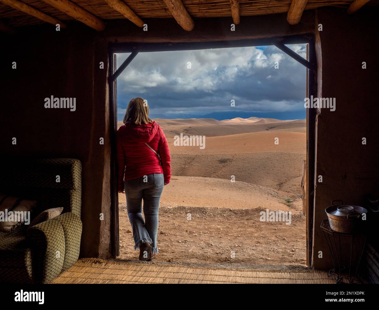 Donna accanto alla porta di una casa marocchina adobe guardando il deserto di Agafay Foto Stock
