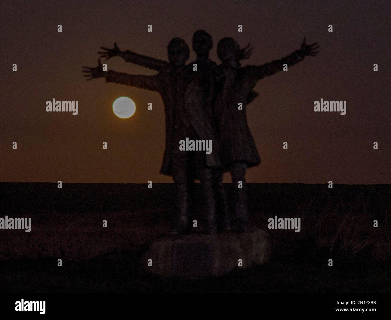 Leysdown, Kent, Regno Unito. 6th Feb, 2023. UK Weather: La Luna di neve visto salire dietro una statua di British Aviation pionieri The Short Brothers - vicino a dove hanno fondato la prima fabbrica di aeroplani al mondo a Leysdown, Kent. Credit: James Bell/Alamy Live News Foto Stock