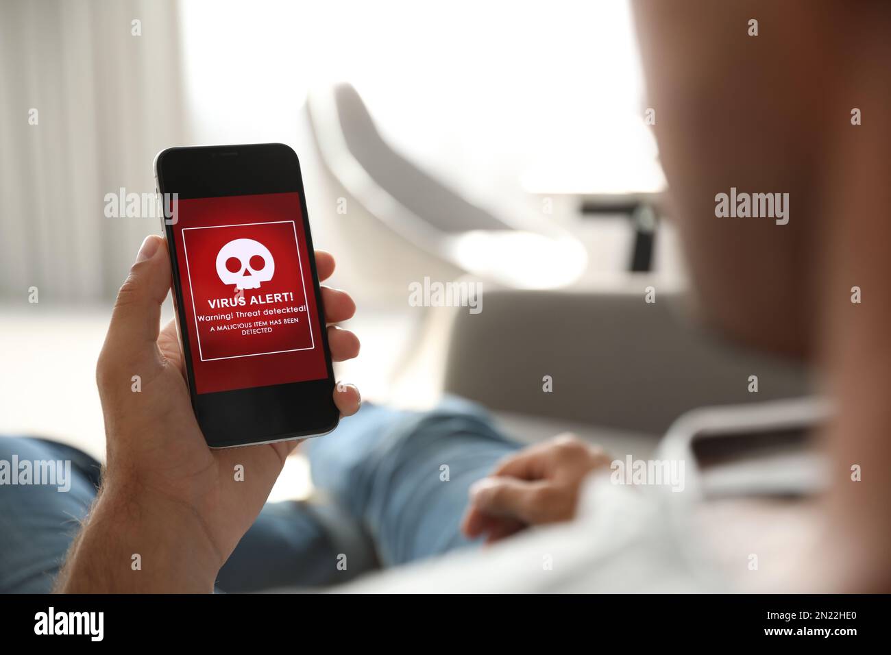 Uomo che tiene in mano lo smartphone con avviso di attacco di virus a casa, primo piano Foto Stock
