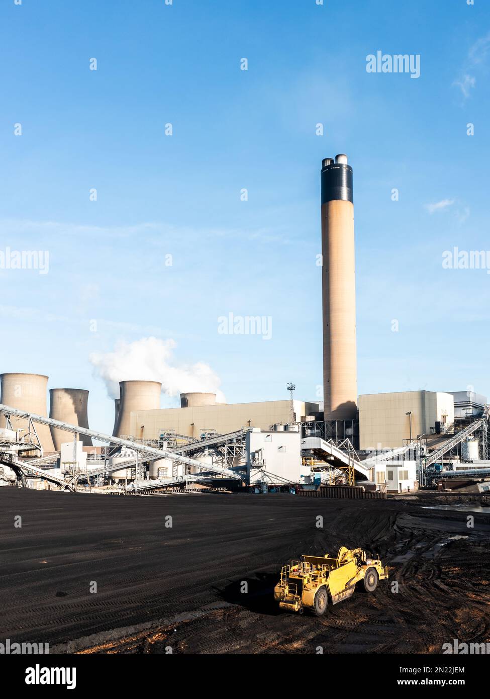 Una macchina pesante che scrapa il carbone da una pila di combustibili fossili in una grande centrale elettrica alimentata a carbone per bruciare per la produzione di elettricità non rinnovabile Foto Stock