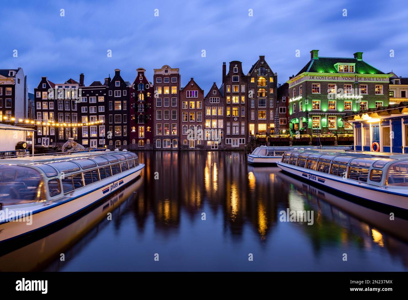 AMSTERDAM, PAESI BASSI - 18 GENNAIO 2023: Paesaggio urbano delle tradizionali case olandesi durante il tramonto sul canale Damrak di Amsterdam Foto Stock