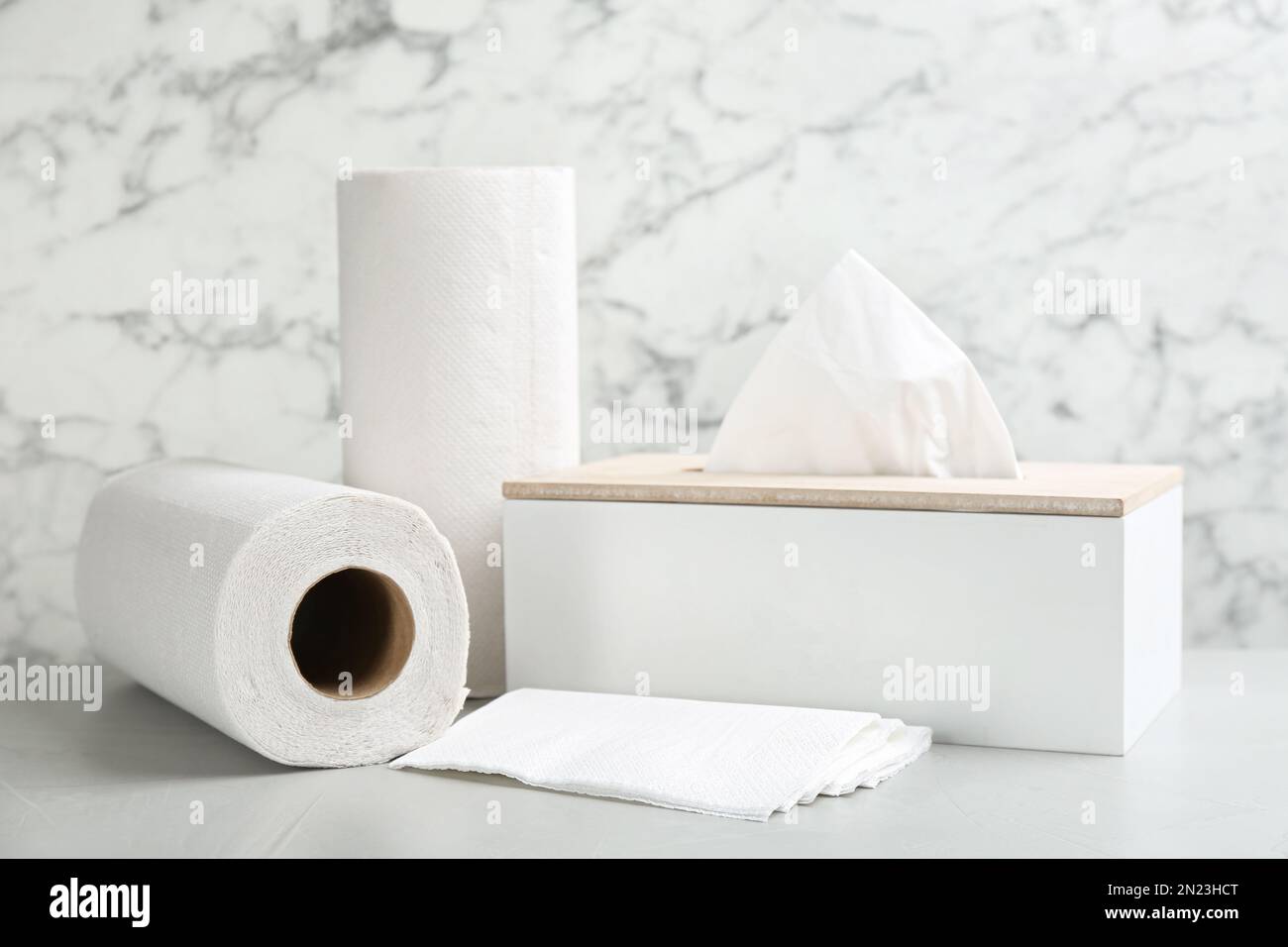 Tovaglioli puliti, scatola con fazzolettini e rotoli di tovaglioli di carta su un tavolo leggero Foto Stock