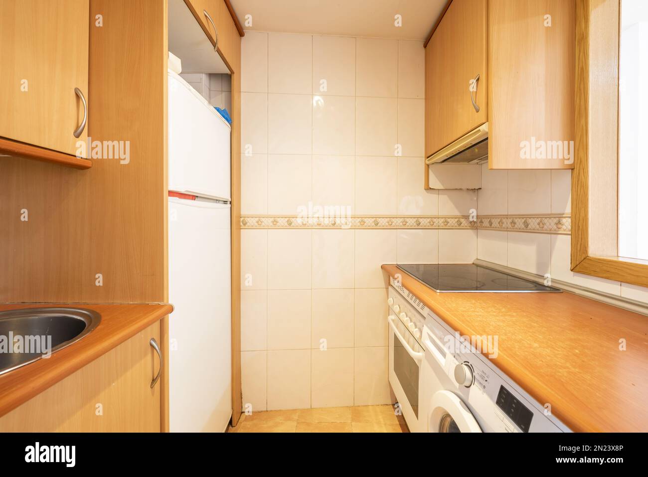 Piccola vecchia cucina con mobili in ciliegio da un appartamento con un portello di servizio e elettrodomestici bianchi Foto Stock