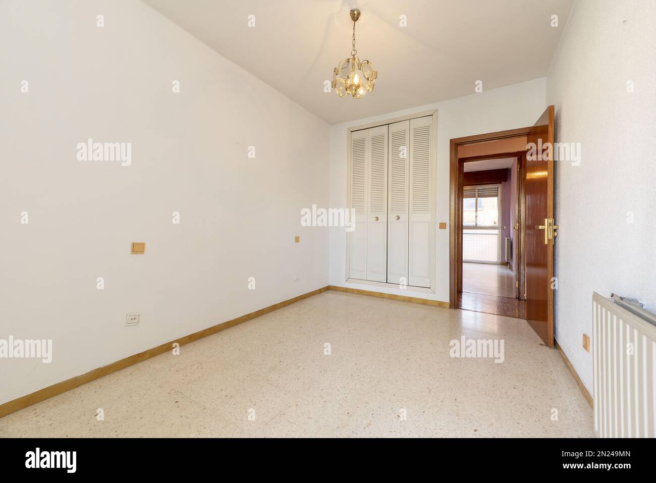 Camera vuota con pareti bianche con armadio a muro con porte bianche pieghevoli in stile veneziano, lampada sospesa al soffitto e porta liscia Foto Stock