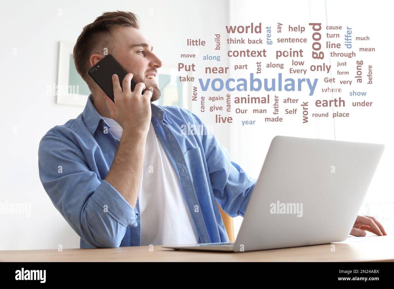 Giovane uomo che parla al telefono cellulare mentre lavora con un computer portatile alla scrivania, parola nuvola davanti a lui Foto Stock