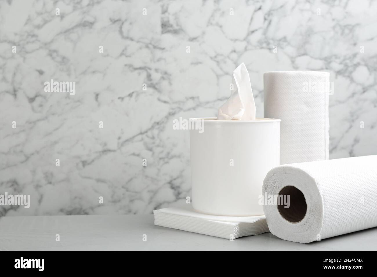 Tovaglioli puliti, scatola con fazzolettini e rotoli di tovaglioli di carta su un tavolo leggero, spazio per il testo Foto Stock