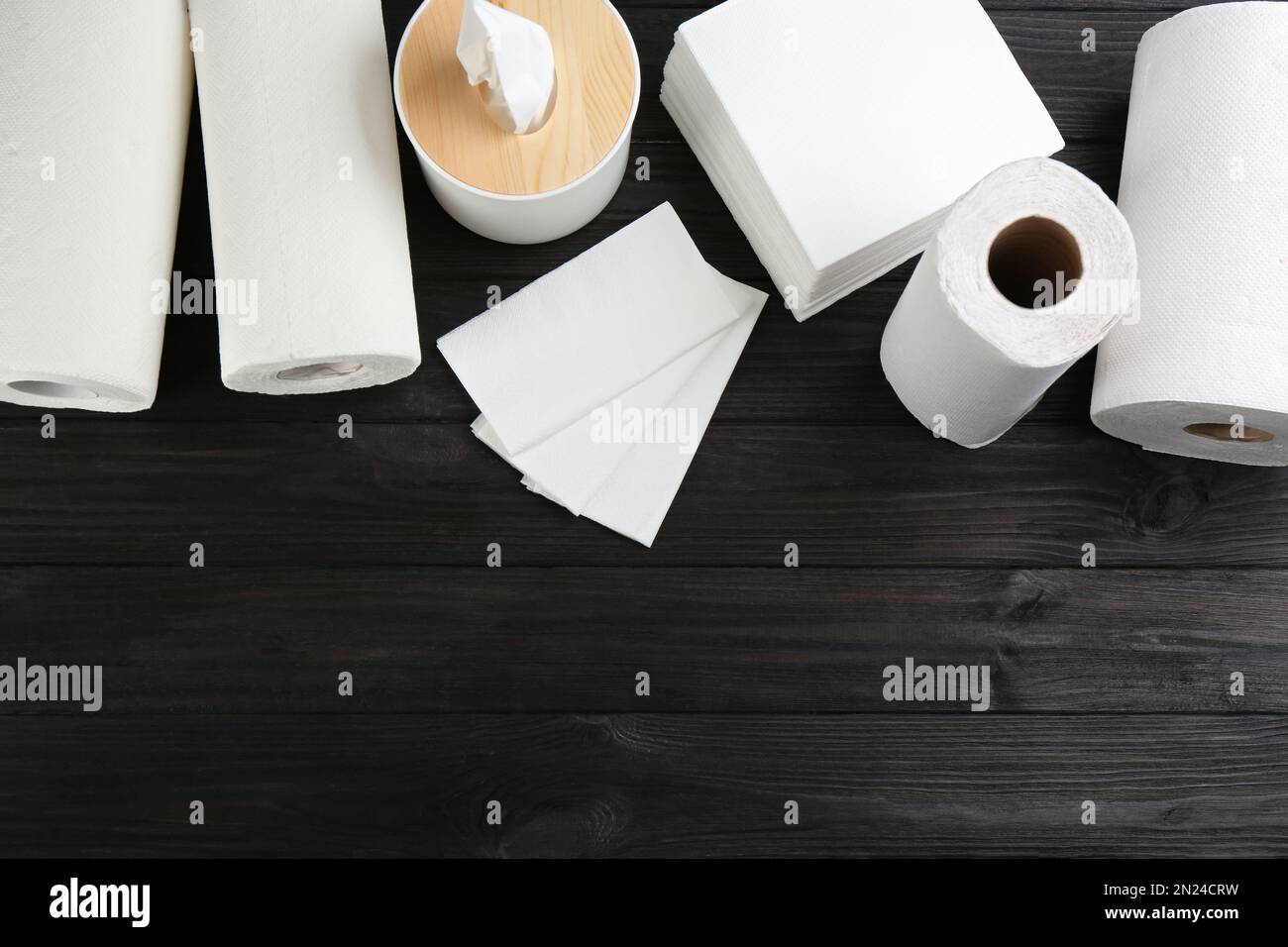 Tovaglioli puliti, scatola con fazzolettini e rotoli di tovaglioli di carta su un tavolo di legno, piatto. Spazio per il testo Foto Stock