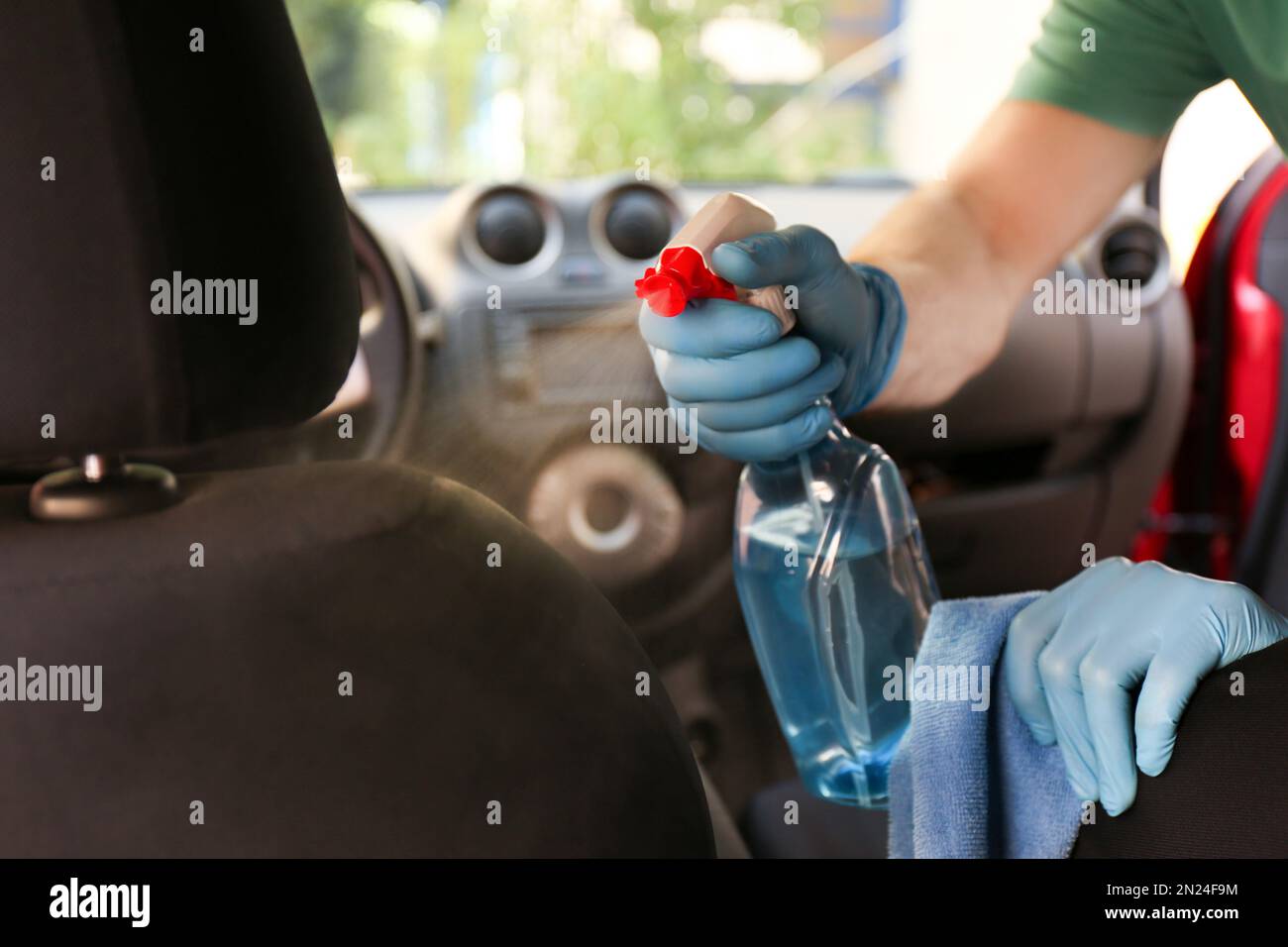 Uomo pulizia salone auto con disinfettante spray e panno, primo piano Foto Stock