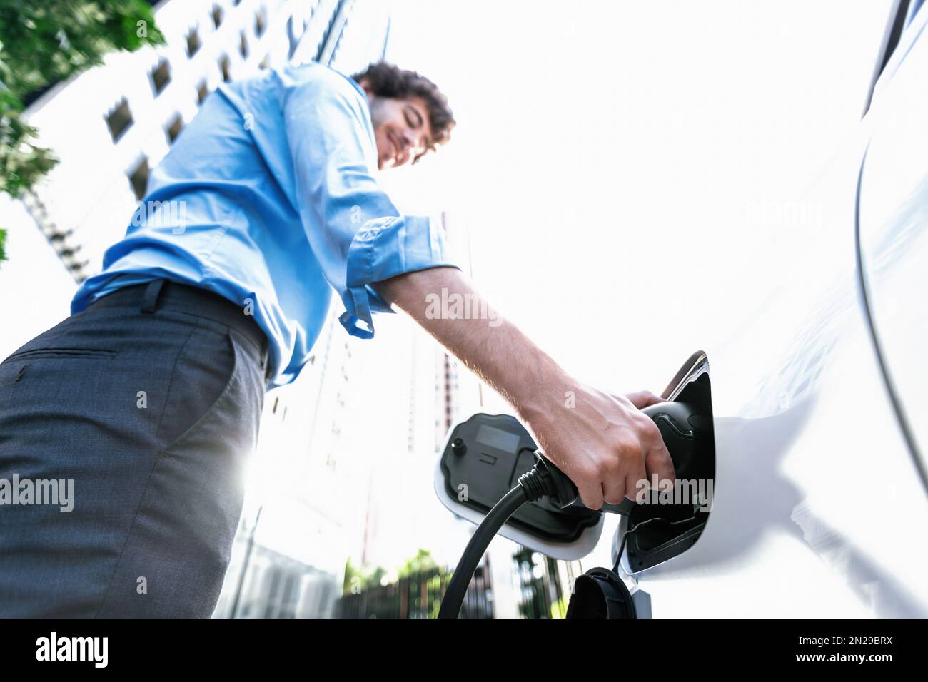 Fisheye vista mettere a fuoco sulla mano inserire il caricabatterie EV spina in auto elettrica con sfondo sfocato di progressive città moderno stile di vita-uomo d'affari ricaricare la sua Foto Stock