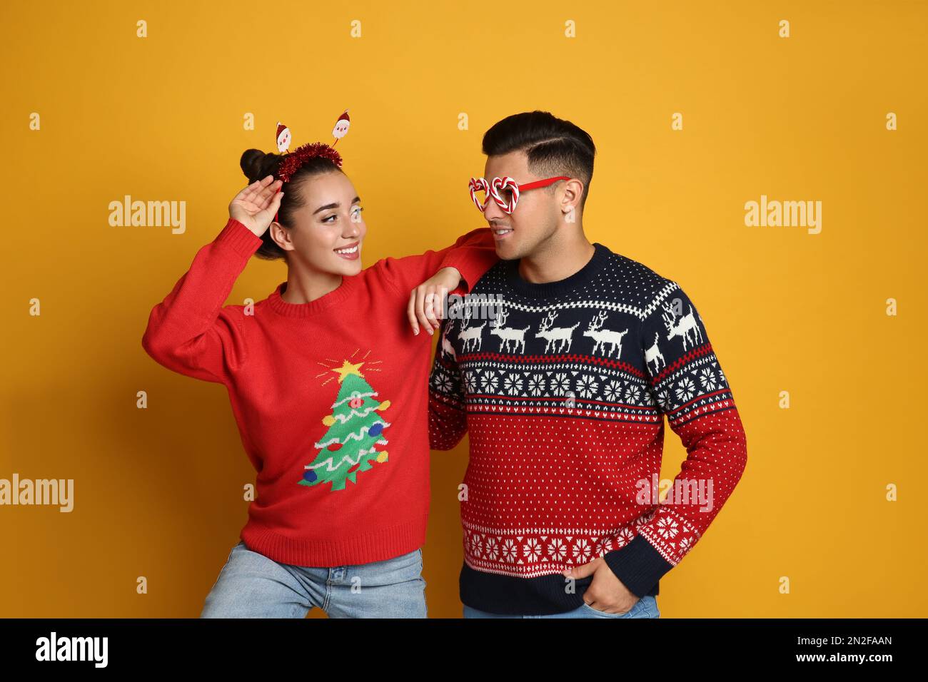 Coppia in maglioni di Natale, fascia di Babbo Natale e occhiali da festa su  sfondo giallo Foto stock - Alamy