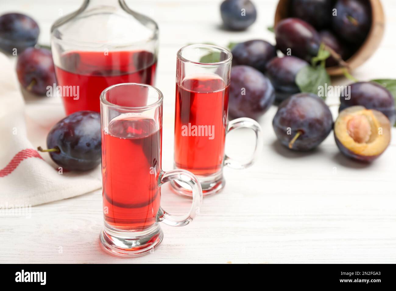 Delizioso liquore di prugne e frutta matura su tavola di legno bianco, primo piano. Bevanda alcolica forte fatta in casa Foto Stock