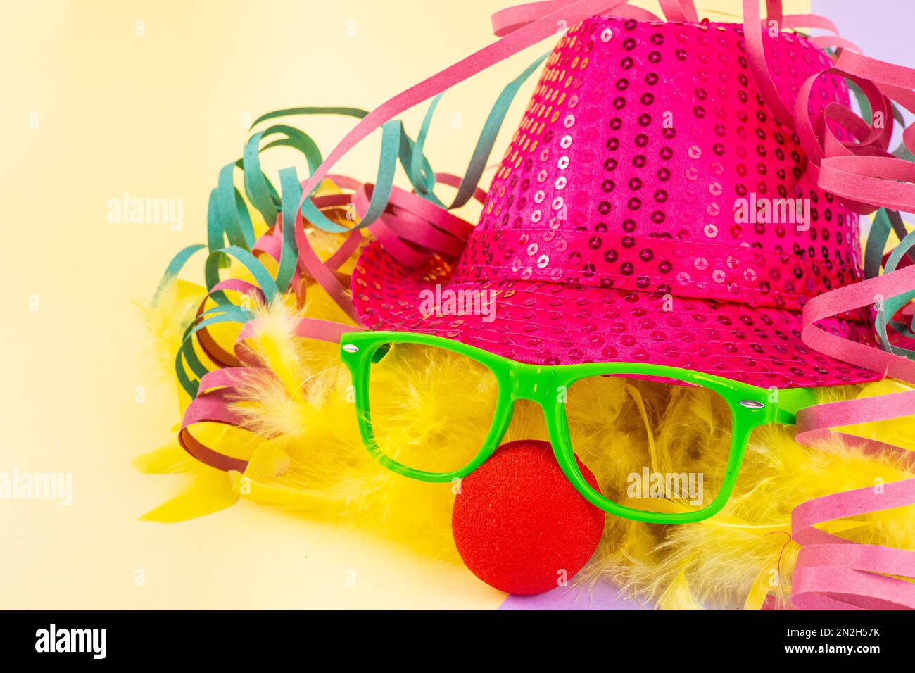 Accessori in costume di Carnevale isolati con sfondo colorato. Cappello  rosa con bicchieri verdi, naso rosso pagliaccio, piume gialle e ruscelli  colorati Foto stock - Alamy