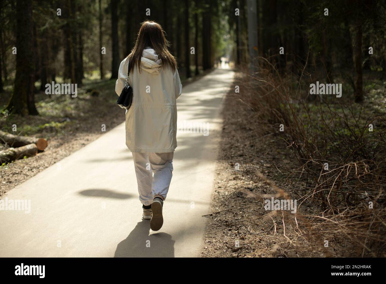 Ragazza in vestiti bianchi cammina attraverso il parco. Donna sul lungo passaggio. Stile moderno di abbigliamento. Foto Stock