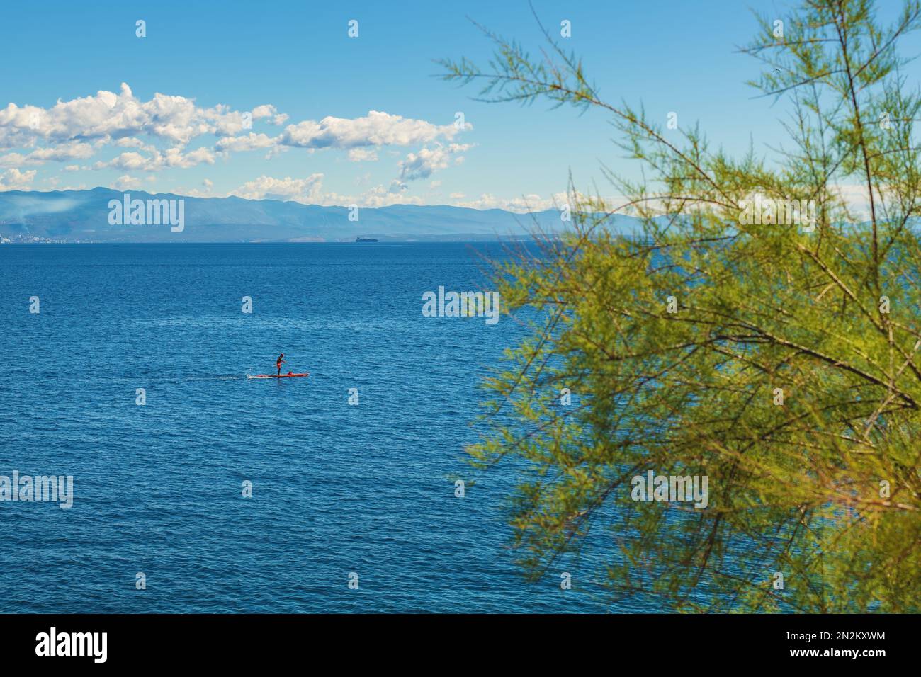 Persona irriconoscibile stand-up paddle boarding sul mare Adriatico Golfo del Quarnero visto dalla costa della città di Lovran, focalizzazione selettiva Foto Stock