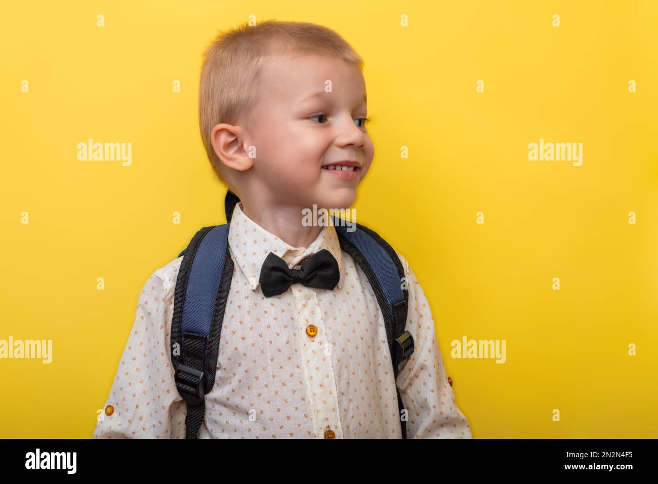 Ritorno a scuola. Un ragazzo biondo sorridente con uno zaino su sfondo giallo guarda via. Istruzione. Banner Foto Stock