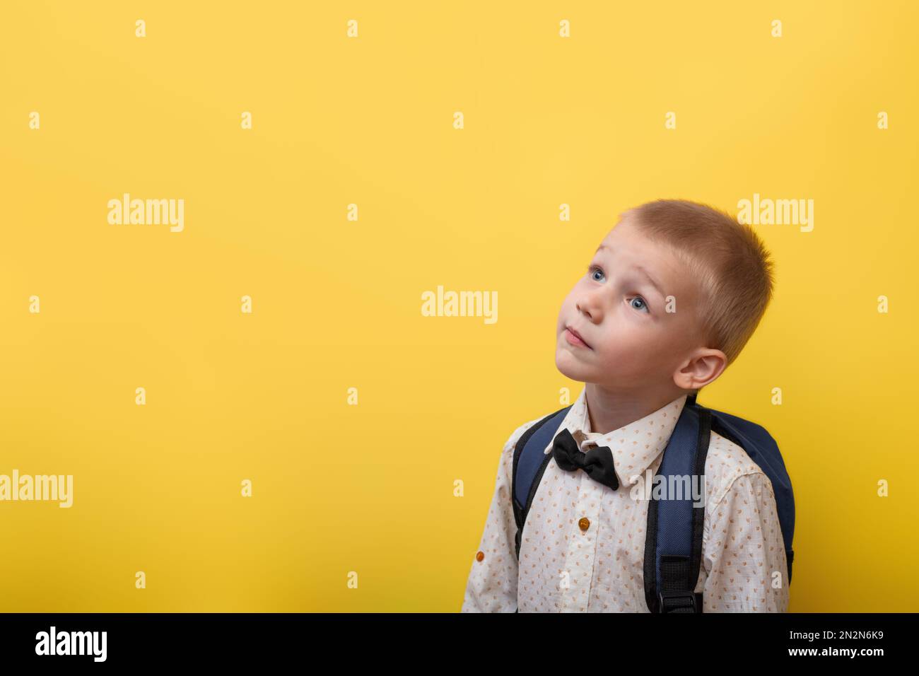 Ritorno a scuola. Un ragazzo biondo con uno zaino in una camicia leggera su sfondo giallo guarda in alto. Istruzione. Banner Foto Stock