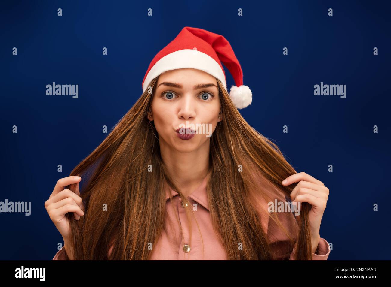 Una ragazza in un cappello di Babbo Natale su uno sfondo blu isolato manda un bacio Foto Stock