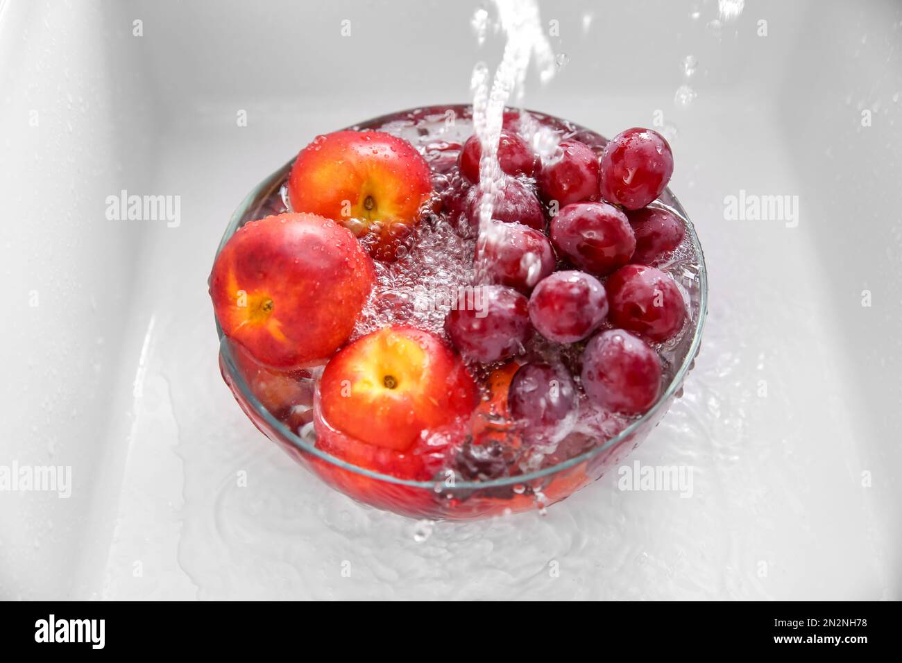 Lavare in ciotola, sotto acqua di rubinetto, uva fresca e nettarine Foto Stock