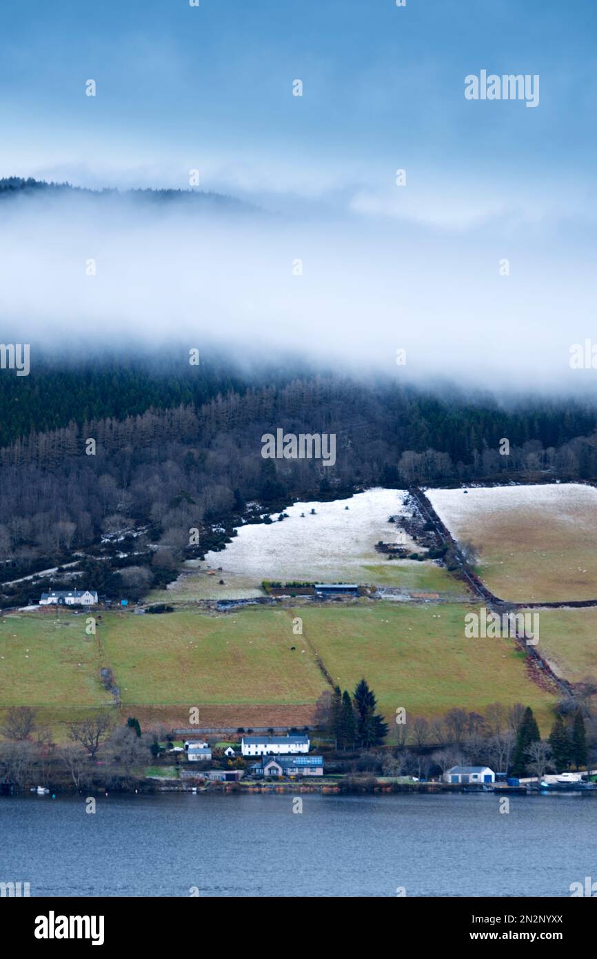 Loch Ness, Highlands, Scozia. Inverno. Montagne, lago e campi parzialmente coperti di neve. Edifici di fattoria, campi, pascoli. Nessuna gente Foto Stock