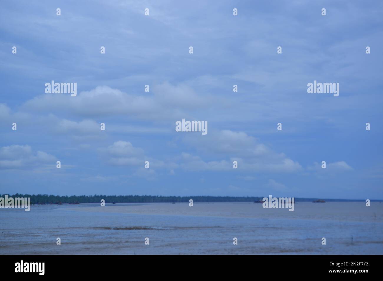 L'acqua di mare sta recedendo con Un cielo azzurro nuvoloso chiaro contro la foresta di Avicennia Marina nel villaggio di Belo Laut nella mattina Foto Stock