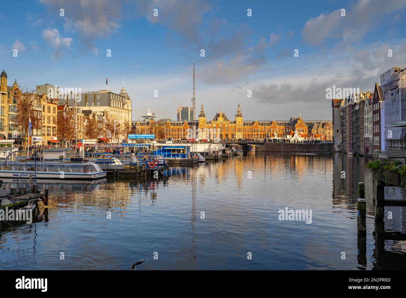 Guardando verso Amsterdam, stazione centrale dal canale Damrak Amsterdam Paesi Bassi. Foto Stock