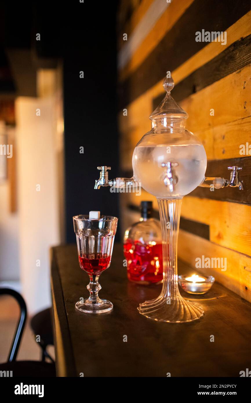 Primo piano di una tradizionale fontana ornata di assenzio con un bicchiere e una bottiglia di liquore rosso Foto Stock