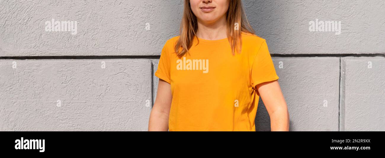 Irriconoscibile donna bionda millenaria in giallo arancione colore T-shirt su sfondo grigio parete Mockup friendly copia spazio per il design e testo urbano coagulo Foto Stock