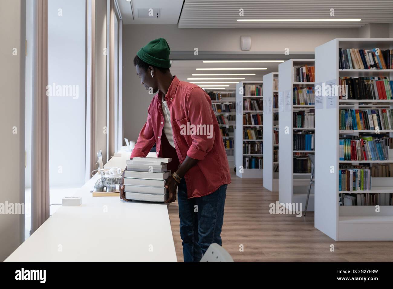 Un giovane diligente uomo afroamericano sta in piedi nella stanza della biblioteca che prepara il rapporto scientifico per l'università Foto Stock