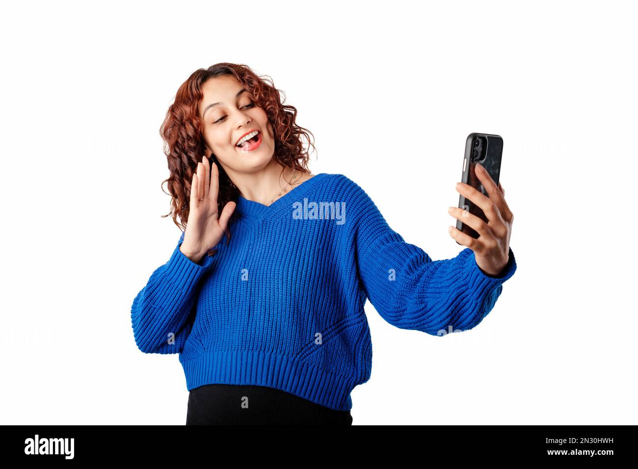 Giovane donna che indossa un pullover blu isolato su sfondo bianco utilizzando lo smartphone per videochiamare. Chat video, conversazione sul telefono cellulare tramite Foto Stock