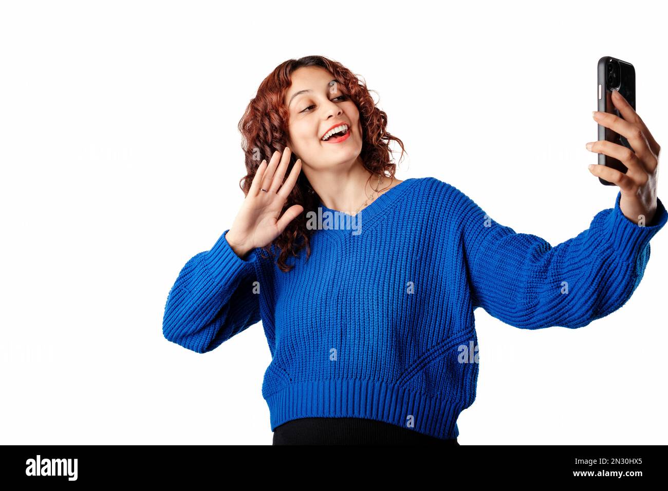 Giovane bella donna che indossa un pullover blu isolato su sfondo bianco utilizzando lo smartphone per videochiamare. Chat video, parlare sul cellulare Foto Stock