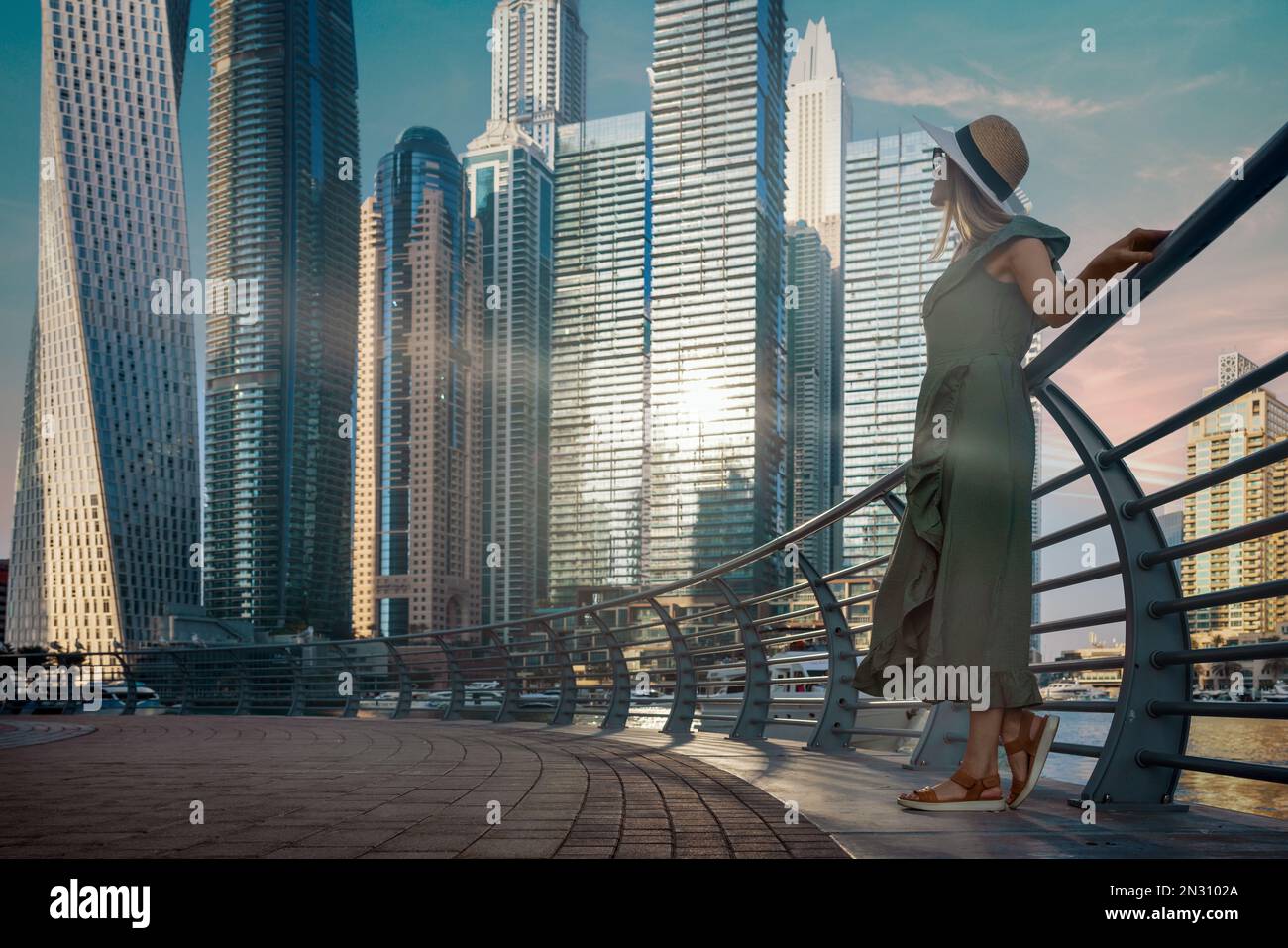 Donna turistica in abiti estivi alla moda e cappello godendosi lo skyline del porto turistico di Dubai al tramonto. spazio di copia Foto Stock