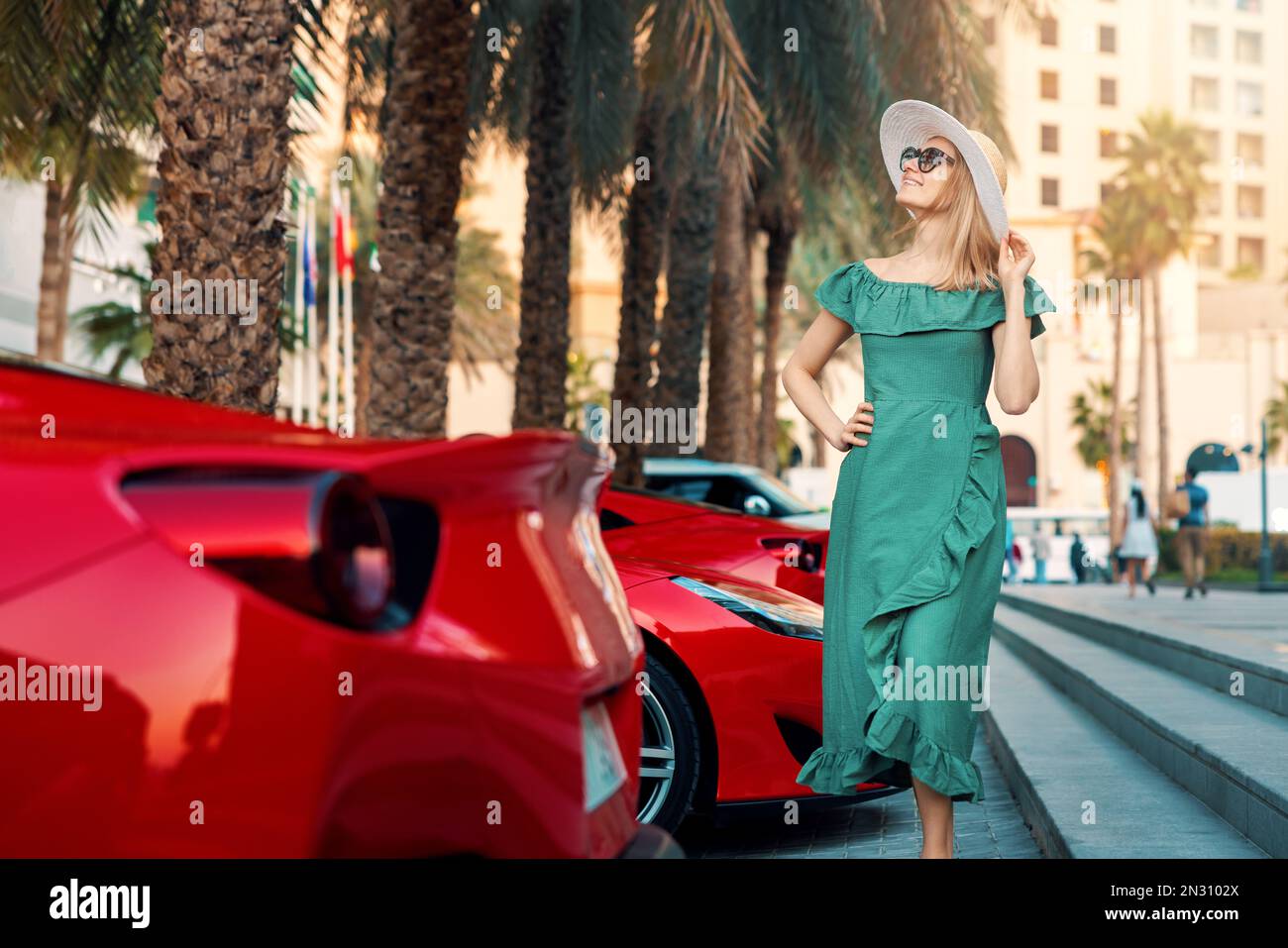 Donna di moda in vestito verde a piedi Dubai città strade. si trova accanto alle auto sportive di lusso. Viaggio negli Emirati Arabi Foto Stock